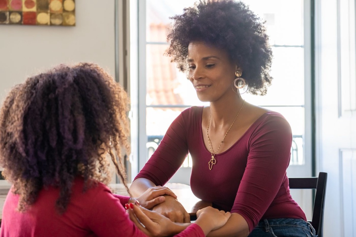 A mother and her teenage daughter talking warmly at a sunlit table